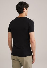 T-shirt noir à manches courtes en coton, avec un col ras du cou classique et une texture lisse, associé à un pantalon beige clair.
