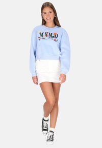 Világoskék, rövidített pulóver virágos hímzéssel és feliratos mintával, fehér miniszoknyával és fekete magas szárú tornacipővel párosítva.