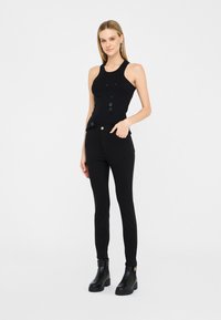 Haut sans manches noir avec des embellissements en perles, associé à un pantalon noir ajusté. Le mannequin porte des bottines noires avec une semelle épaisse.