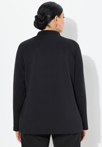 Svart långärmad topp i slätt tyg; har en enkel krage, rak snitt och minimal sömnad. Styling med matchande byxor.