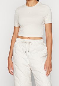 Beżowy krótki t-shirt z krótkimi rękawami i małym białym logo Nike, zestawiony z teksturowanymi, lekkimi kremowymi pikowanymi spodniami dresowymi.