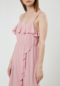 Vestido sin mangas de color rosa con escote con volantes y un volante lateral, que cuenta con una cintura elástica para un ajuste ceñido. Tejido suave y ligero.