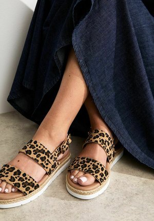 Sandalias de estampado de leopardo con dos tiras anchas, una suela estilo espadrille y una base de goma blanca; combinadas con una falda de mezclilla oscura.