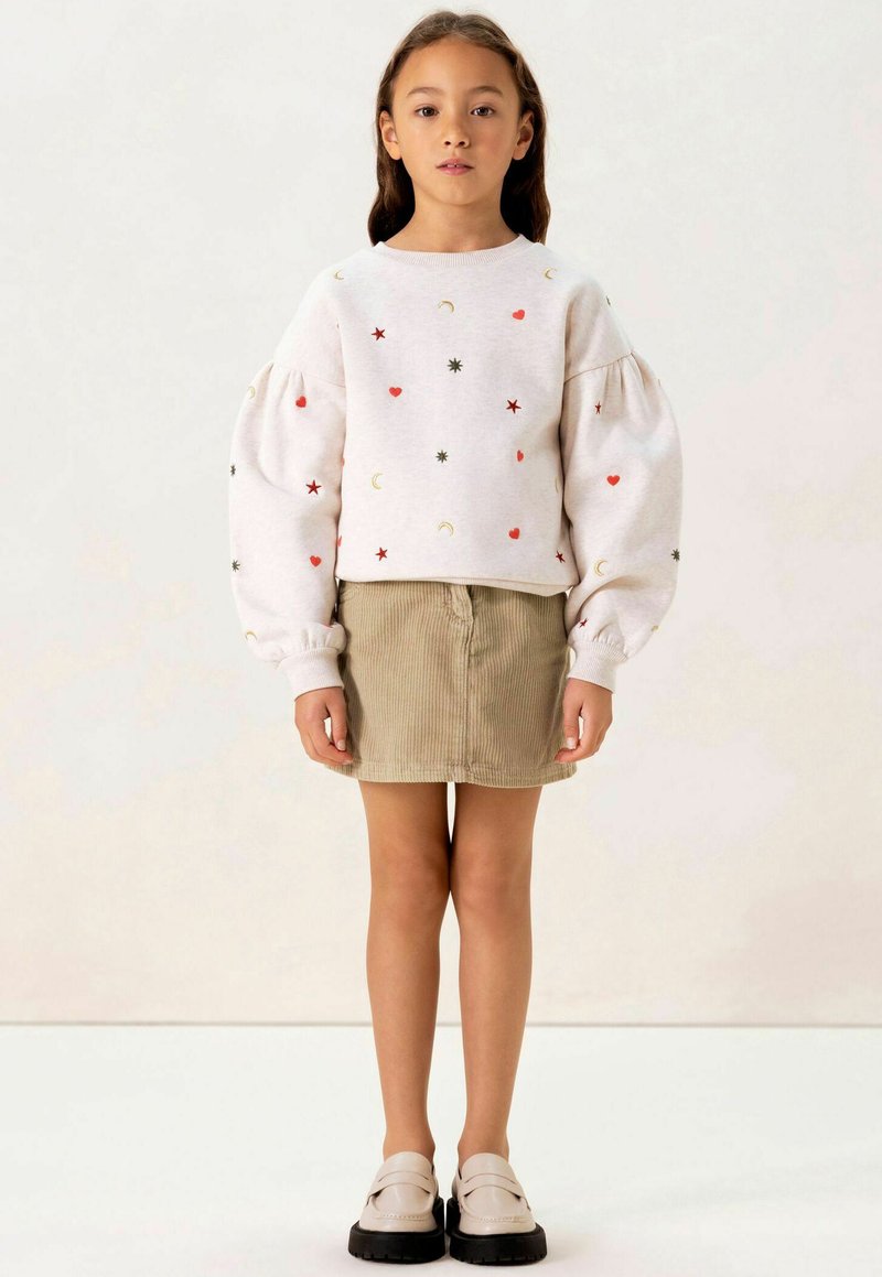 Sweat-shirt bleu clair brodé avec des manches bouffantes, orné d'étoiles, de cœurs et de lunes. Assorti à une jupe mini en velours côtelé beige et des chaussures noires.