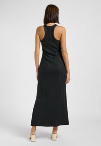 Abito maxi nero a costine con design senza maniche e silhouette aderente. Presenta un collo rotondo e un orlo lungo e dritto.