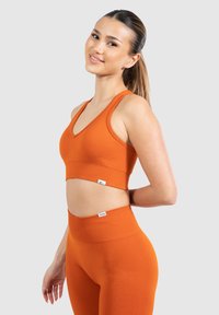 Sujetador deportivo naranja de canalé con escote en V, combinado con leggins de cintura alta a juego. El material parece elástico y ajustado.