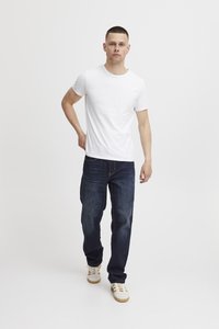 Camiseta blanca de manga corta combinada con jeans azul oscuro y zapatillas blancas. El conjunto presenta un ajuste casual con un diseño minimalista.