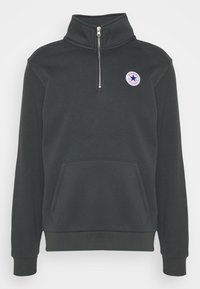 Sudadera gris oscuro con cuello alto y medio zipper, que cuenta con un bolsillo frontal tipo canguro y un logo circular en el pecho.