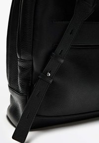 Borsa in pelle nera con superficie testurizzata, dotata di una lunga tracolla e di accessori metallici. Cuciture visibili e una base liscia e arrotondata.