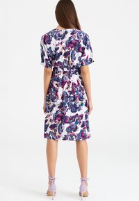 Sukienka w kwiaty z białym tłem oraz wzorami w odcieniach fioletu i niebieskiego, krótkimi rękawami, elastyczną talią i długością do kolan.