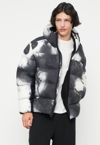 Jachetă cu umplutură, în alb și negru, cu un design de stropi. Dispune de glugă, fermoar frontal și manșete elastice. Material texturat, căptușit.