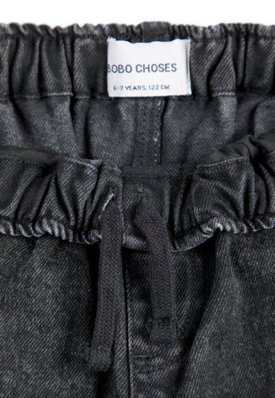 Shorts de mezclilla gris con cintura elástica y cordón negro. La etiqueta dice "BOBO CHOSES, 6-7 años, 122 cm." Textura suave.