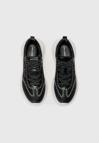 Baskets noires avec une texture, des accents de couture blanche, un bout arrondi et une semelle extérieure blanche épaisse. Design à lacets, logo visible.