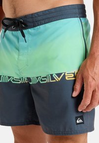 Męskie kąpielówki z gradientowym wzorem przechodzącym od jasnej zieleni do ciemnego niebieskiego, elastyczny pas ze sznurkiem oraz akcentem logo.