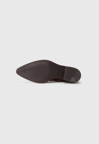 Semelle de chaussure en cuir marron avec une forme pointue, dotée de motifs de traction en caoutchouc et d'un logo subtilement estampillé près du talon.