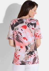 Haut à manches courtes en tissu léger, arborant un motif floral vibrant dans des tonalités de rose, rouge, noir et beige, avec une coupe décontractée.