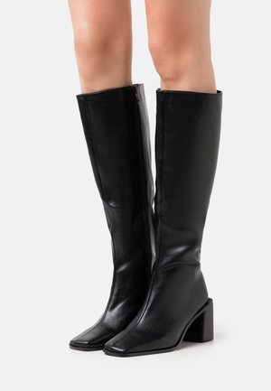 Zwarte laarzen tot de knie van glanzend leer met een vierkante neus en blokhak. Voorzien van een rits aan de zijkant voor gemakkelijke instap.