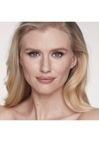 Headshot of a person with long, wavy blonde hair, blue eyes, and natural makeup, featuring a smooth complexion and neutral lip color.