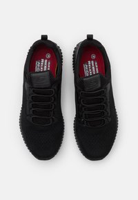 Black athletic shoes with a mesh upper and elastic bands instead of traditional laces. Textured rubber soles and red insoles are visible.