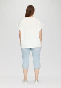Lässiges weißes T-Shirt mit kurzen Ärmeln, kombiniert mit hellblauen, cropped Jeans. Die Schuhe haben silberne Akzente. Glatte Stofftextur.