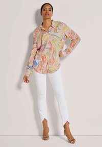 Mehrfarbiges Hemd mit Knopfleiste und wirbelnden Mustern in Pastellfarben, kombiniert mit weißen Skinny-Jeans mit ausgefranstem Saum.