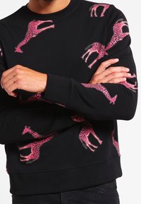 Sudadera negra con estampado repetido de jirafas rosas, cuello redondo, mangas largas y dobladillo y puños acanalados. Material suave de mezcla de algodón.