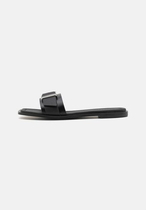 Schwarze Rutschsandale mit flacher Sohle und zwei Riemen. Verfügt über einen strukturierten oberen Riemen mit einem dekorativen Hardware-Akzent. Insgesamt glatte Oberfläche.