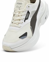 Puma sneakers med en vit mesh-överdel, svarta accenter och en texturerad mellansula. Har en vadderad tunga och kontrasterande overlay.