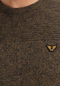 Pull en maille marron et gris foncé avec un motif texturé, col rond, et un petit logo noir et doré sur le côté gauche.