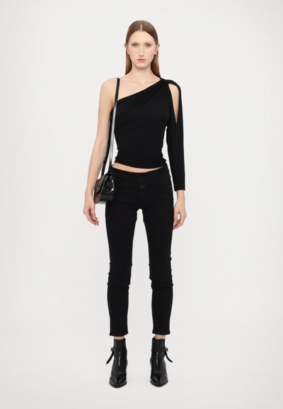 Svart asymmetrisk topp med én langärm, kombinert med svarte skinny jeans og ankelstøvletter. Inkluderer en liten svart crossoverveske.