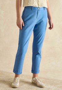 Jasnoniebieskie spodnie o prostym kroju wykonane z mieszanki bawełny, z zapięciem na guziki i podwiniętymi nogawkami. W zestawie z beżowymi sneakersami.