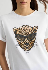 T-shirt bianca con un'illustrazione di un viso di leopardo che indossa occhiali da sole, dettagliata con macchie nere e marroni, e il nome del brand "LIU-JO" sotto.