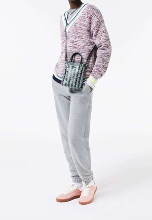Knitted pullover in pink and white, gray sweatpants, and pink sneakers. Small green patterned handbag hangs from shoulder.