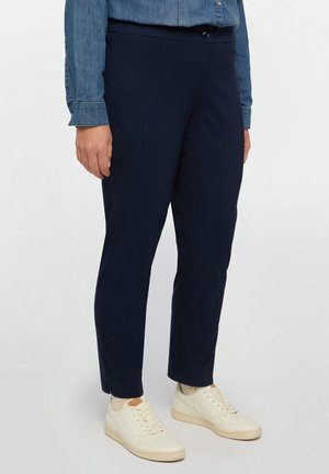 Pantaloni blu navy slim-fit con una texture liscia, dotati di chiusura con bottone e cuciture laterali. Abbinati a sneakers beige.