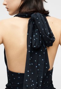 Γυναίκα που φοράει μαύρο φόρεμα χωρίς πλάτη με ανοιχτό μπλε πουά, με ένα μεγάλο φιόγκο δεμένο στο πάνω μέρος της πλάτης.