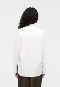 Λευκό πουκάμισο μακρυμάνικο με ευθύ κόψιμο, μανσέτες με κουμπιά και υφή χωρίς τσακίσεις. Διαθέτει πίσω πέτο και λείο ύφασμα.