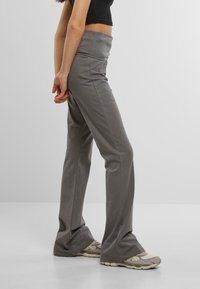 Pantaloni grigi a gamba larga realizzati in un tessuto morbido con vita alta e cuciture laterali, abbinati a scarpe da ginnastica beige. Tessuto liscio, design informale.