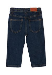 Jean en denim bleu foncé avec deux poches arrière, coutures contrastées et un patch logo en cuir marron à la taille. Coupe droite.