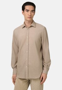 Beige langwerpige blouse met lange mouwen, gemaakt van lichte stof, met een kraag, knoopsluiting en een rechte pasvorm.