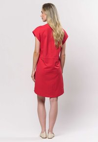 Rochie roșie cu mâneci scurte, confecționată din material moale, cu croială lejeră și tiv rotunjit. Are o cusătură centrală în spate și un design simplu.