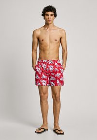 Shorts de bain rouges avec des motifs floraux bleus, taille élastique, cordon de serrage et poches latérales, fabriqués en matériau léger.