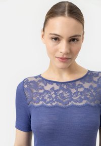 Paarse geribde top met een doorschijnend kantpaneel met bloemmotieven langs de halslijn. Korte mouwen, een soepele textuur en een getailleerd ontwerp.