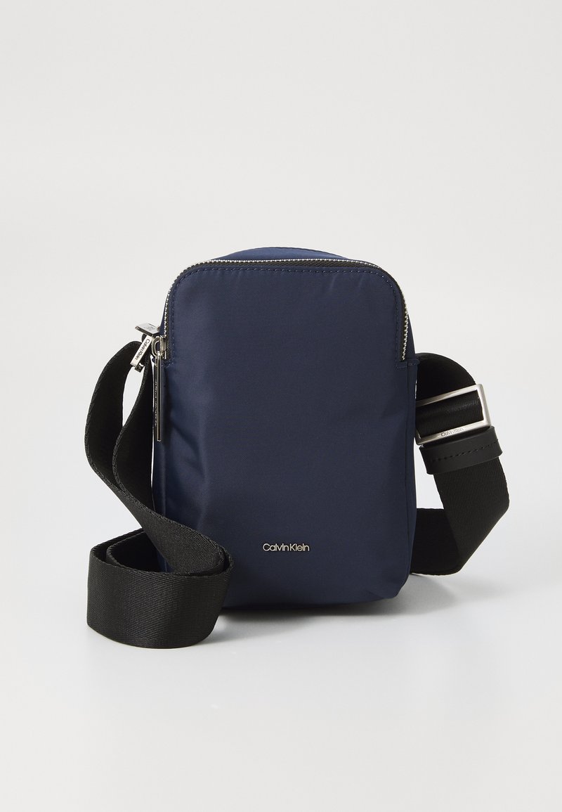 Borsa a tracolla in nylon blu marina con chiusura a zip, tracolla nera regolabile, hardware argentato e logo Calvin Klein sul davanti.