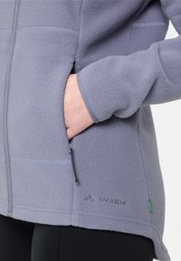 Fleecejacke in hellem Lavendel mit weicher Textur, mit Reißverschlusstaschen und einem Logo am Saum. Verfügt über eine taillierte Passform und kontrastierende Nähte.