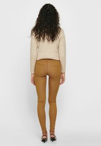 Bruine slim-fit broek met een hoge tailleband, achterzakdetails en een gladde textuur, gecombineerd met een lichtbeige sweater.