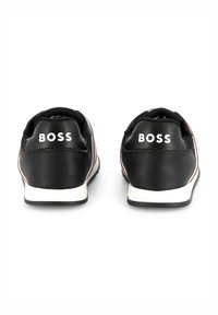 Black sneakers with white accents and "BOSS" logo on the back. Made of smooth leather with a textured upper and a contrasting white sole.