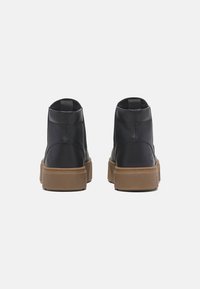 Stivaletti in pelle nera alla caviglia con suola spessa beige, dotati di linguetta e cuciture visibili sul retro. Texture liscia e design minimalista.