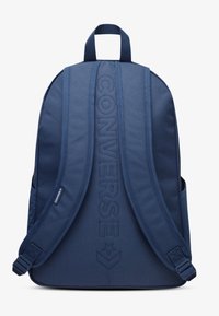 Sac à dos bleu marine en tissu texturé, avec logo "CONVERSE" embossé, bretelles rembourrées et poches latérales pour le rangement.