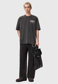 Koksgrå oversized T-shirt med hvidt og rødt logo, kombineret med sorte viddeben jeans og en sort tote taske med justerbare stropper.
