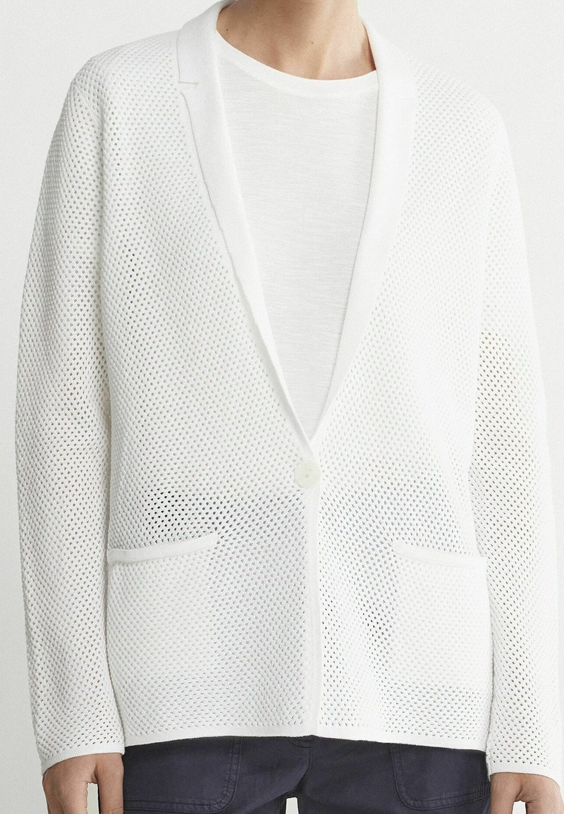 Blazer blanc en maille filet avec tissage ouvert, col châle, fermeture à un bouton et deux poches avant. Tissu texturé et coupe moderne.